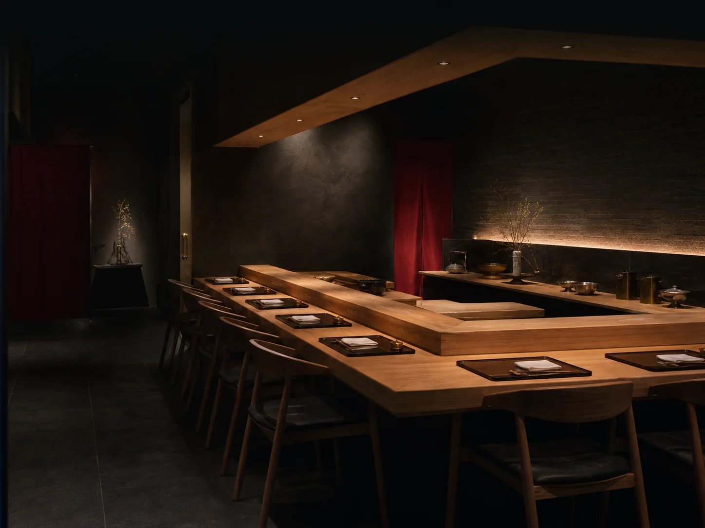 Un counter japonez intim, cu lemn cald și accente bordo, într-un interior întunecat